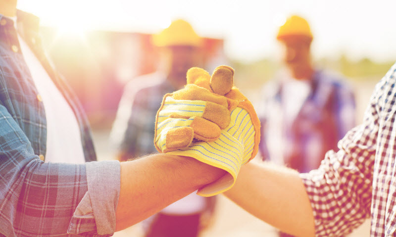 builders hands in gloves greeting each other with handshake on construction site